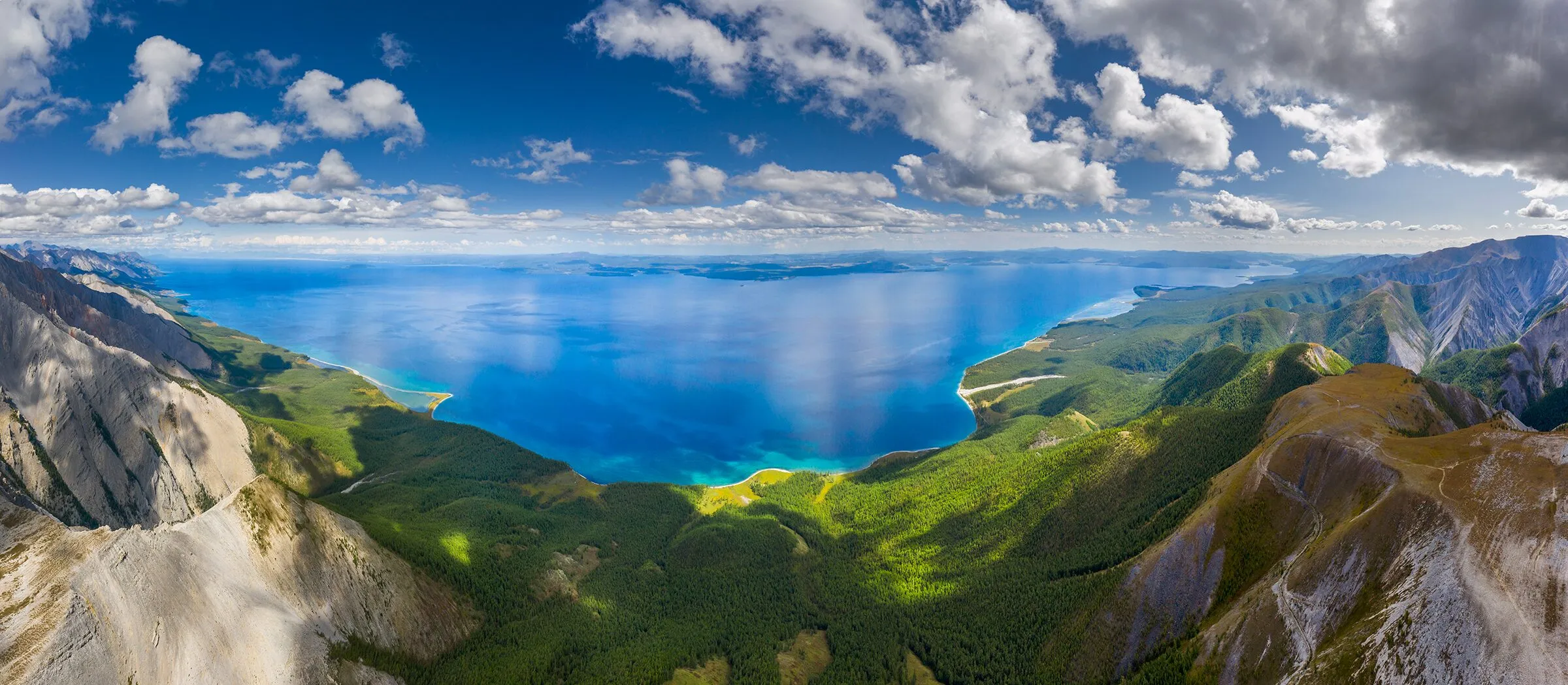 蒙古北部森林群山间的深蓝色湖泊鸟瞰全景，积云在天空缓缓飘过。